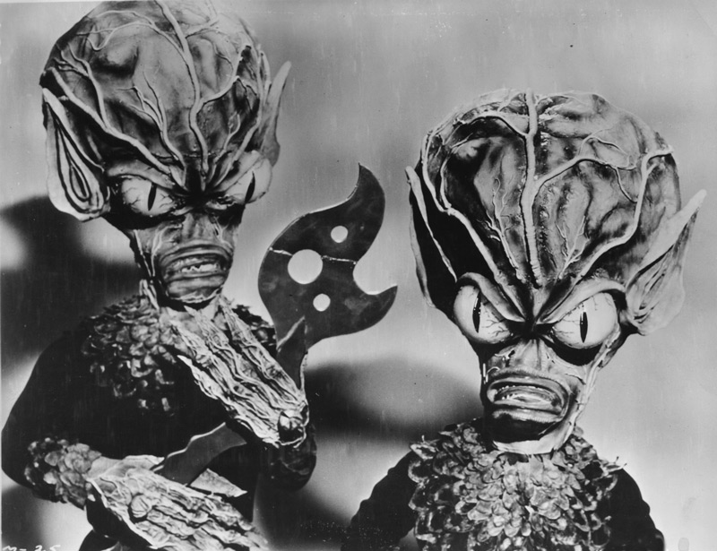 Invasion of the Saucer Men, 1957, motion picture, AIP.  A publicity photo of the Saucer Men.  The actor on the left holds a tool fashioned by Paul Blaisdell out of balsa wood and painted to look like metal.  Blaisdell cautioned the cast that the prop was extremely fragile, but one of them managed to break it anyway.  The tool never appeared in the finished film because of the mishap, but is preserved here in this photograph, with the hastily repaired break clearly visible. Click to enlarge.