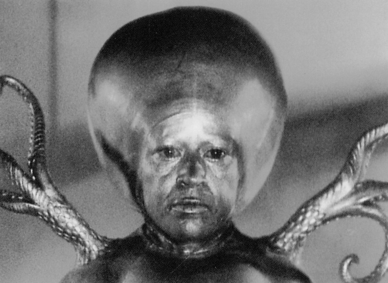 A view of the Martian Intelligence from Invaders from Mars.  Actress Luce Potter, a midget, played the Martian Intelligence in close-ups.  Without the benefit of dialogue, Ms. Potter's eyes are the only means of expressively conveying the strange aloofness of this otherworldly character.  The brothers Howard and Theodore Lydecker molded the brontocephalic dome of the creature and its atrophied body in rubber.  The tentacles were operated by grips with wires positioned beyond the range of the camera and a special gold metallic make up was formulated by cosmetics expert Anatole Robbins and applied by make up artist Gene Hibbs. Click to enlarge.