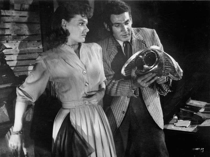 Sylvia van Buren (Ann Robinson) and Clayton Forrester (Gene Barry) look at a Martian electronic probe after Forrester has severed it from the metal stalk on which it was attached.  The probe was released through a door in the underbelly of a Martian war machine during a tense scene in George Pal's film version of The War of the Worlds. Click to enlarge.