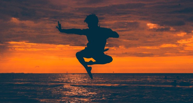 Silhoutte of a figure leaping in a stereotypical martial arts pose against a sunset sky