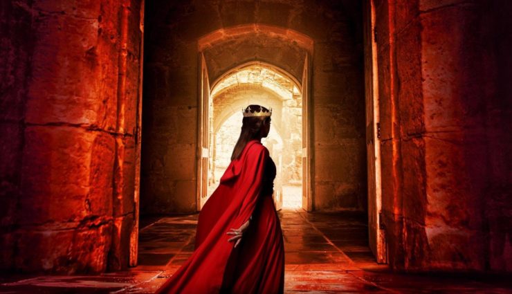 Image of a woman in a red gown and cape, wearing a crown, silhouetted against an open doorway