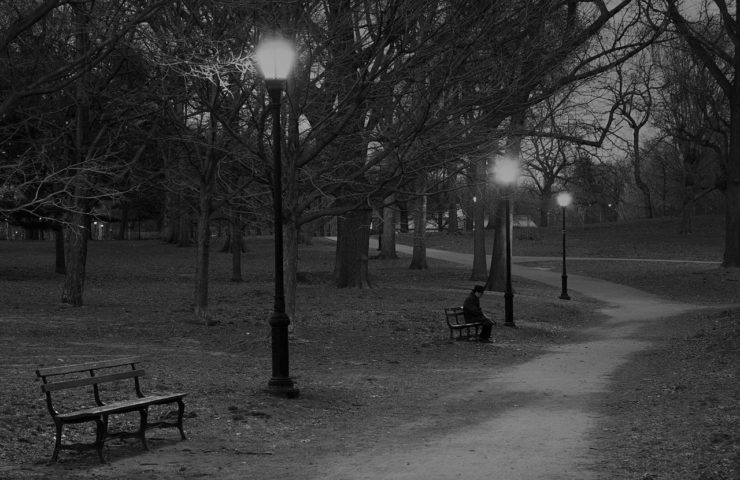 Photo of a man sitting alone on park bench at night.