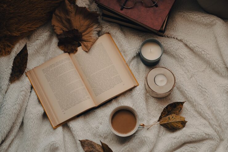 Photograph of an open book on a blanket, surrounded by autumn leaves