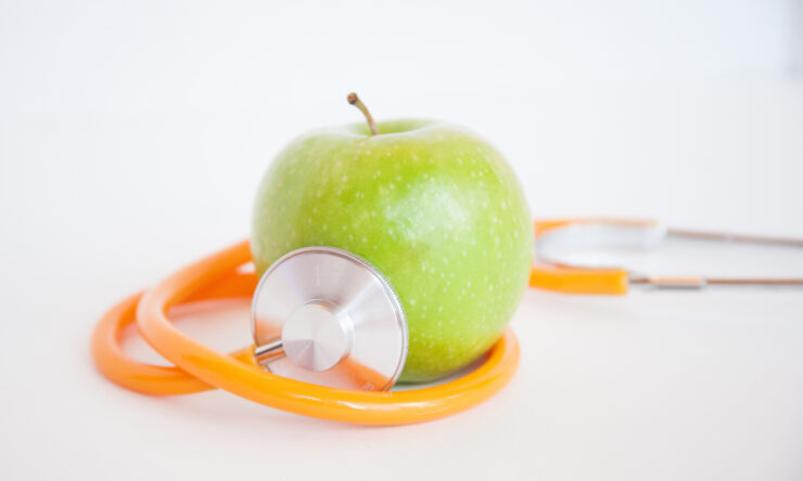 Photograph of a stethoscope wrapped around a green apple against a white backdrop