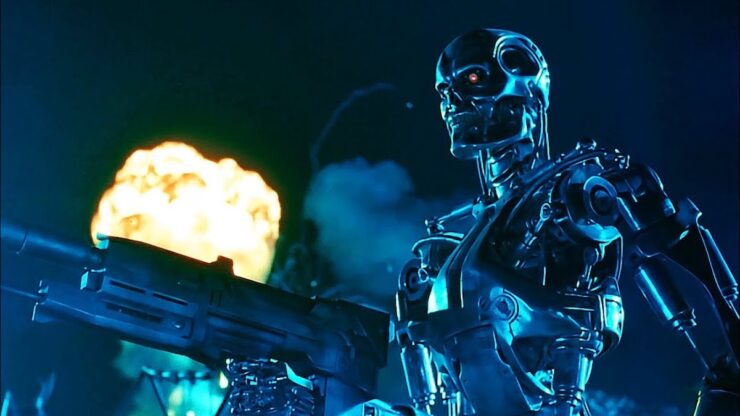 Scene from Terminator 2: Judgment Day: A T-800 model terminator holds a machine gun; a fiery explosion is visible in the background.