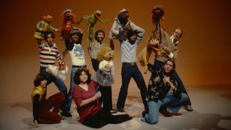 Jim Henson and fellow puppeteers holding Muppets aloft