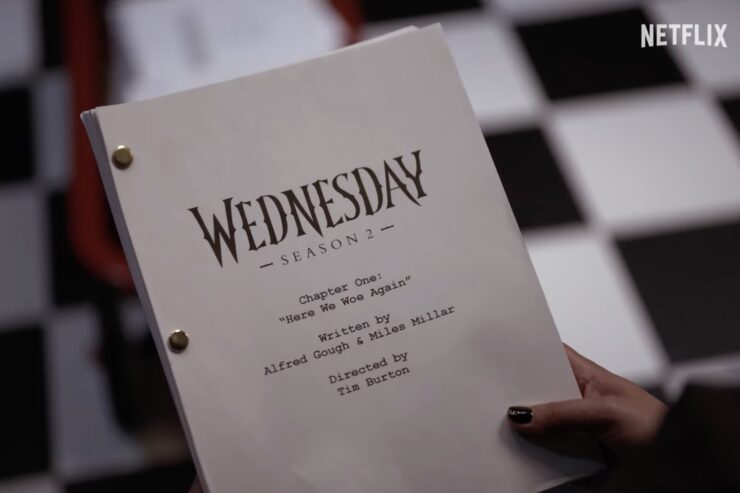 A hand holds a script for Wednesday that shows the season-two premiere title is "Here We Woe Again"