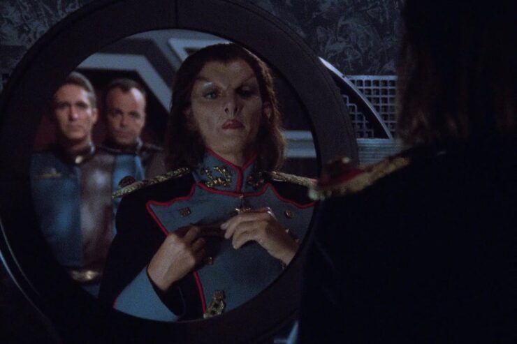 A scene from Babylon 5 "Deathwalker": Jha’dur adjusts her uniform in a mirror, while Captain Sinclair and Garibaldi stand in the background.