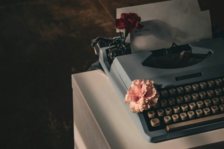 Photo of a typewriter in shadow, with two flowers placed on the keys and in the carriage return