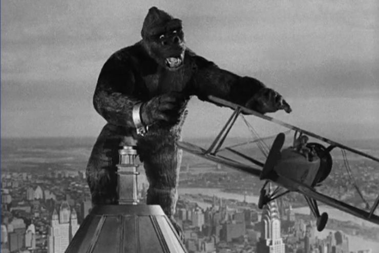 Scene from King Kong (1933): King Kong stands atop the Empire State Building and attempts to grab a passing biplane.