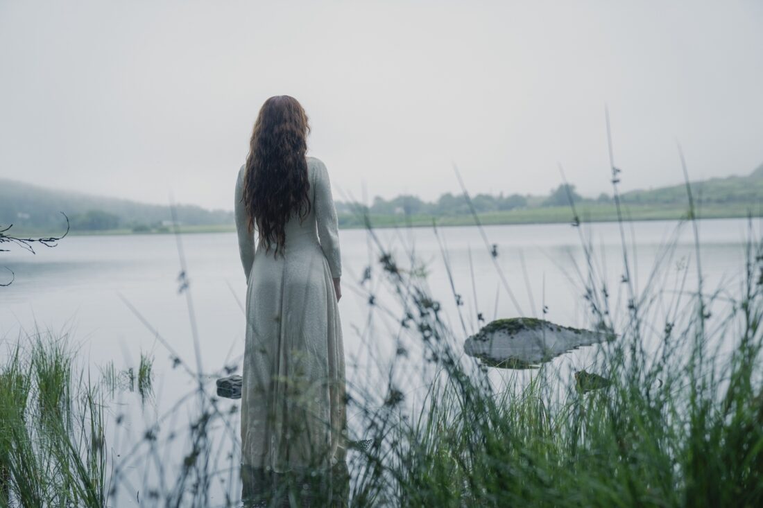 A scene from House of the Dragon, season 2 episode 7: Alicent (Olivia Cooke) stands at the edge of a lake.