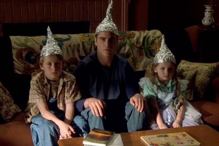 A scene from the movie Signs (2002): Morgan (Rory Culkin), Merrill (Joaquin Phoenix) and Bo (Abigail Breslin) sit together on the couch wearing tin foil hats.