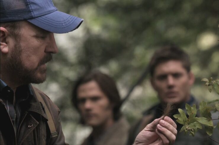 A scene from Supernatural's “How to Win Friends and Influence Monsters”: Bobby Singer investigates a bit of fur, with Sam and Dean in the background.