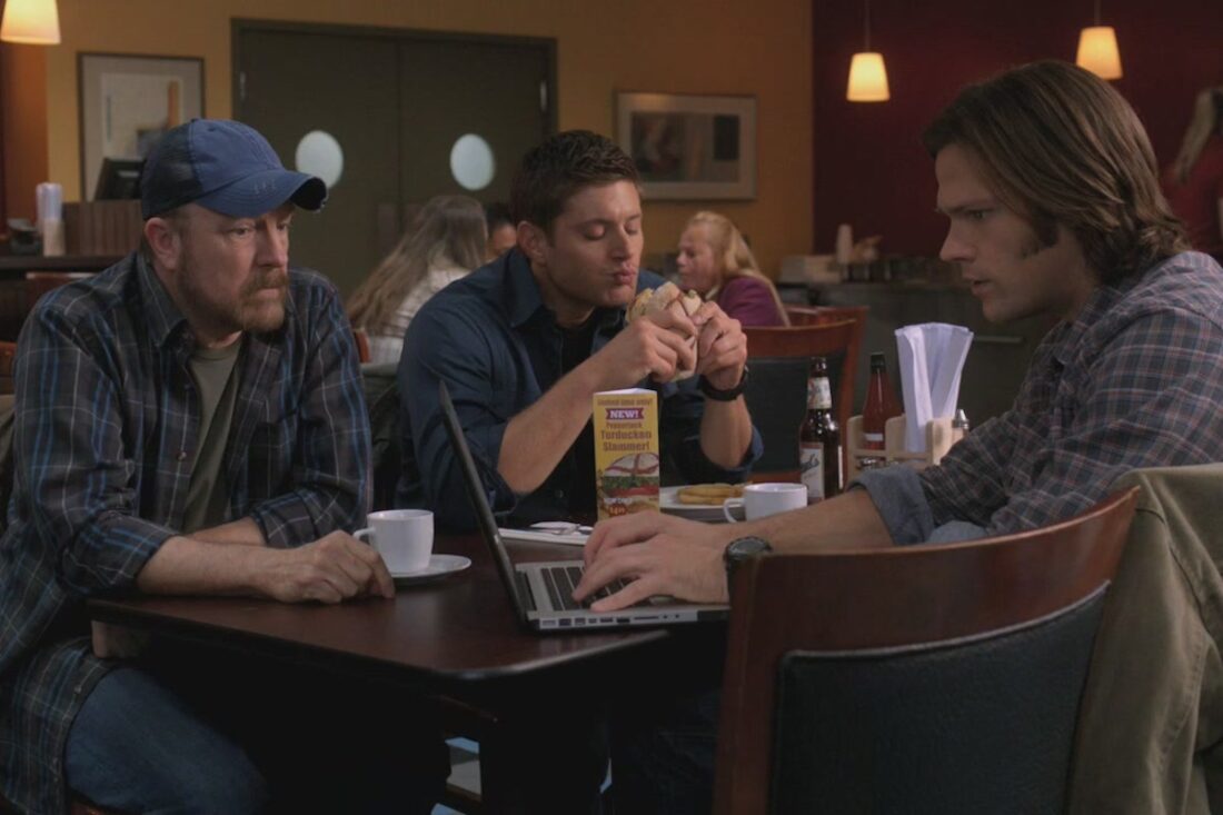 A scene from Supernatural's “How to Win Friends and Influence Monsters”: Bobby Singer, Sam, and Dean at a restaurant; Dean eats a "Turducken Slammer"