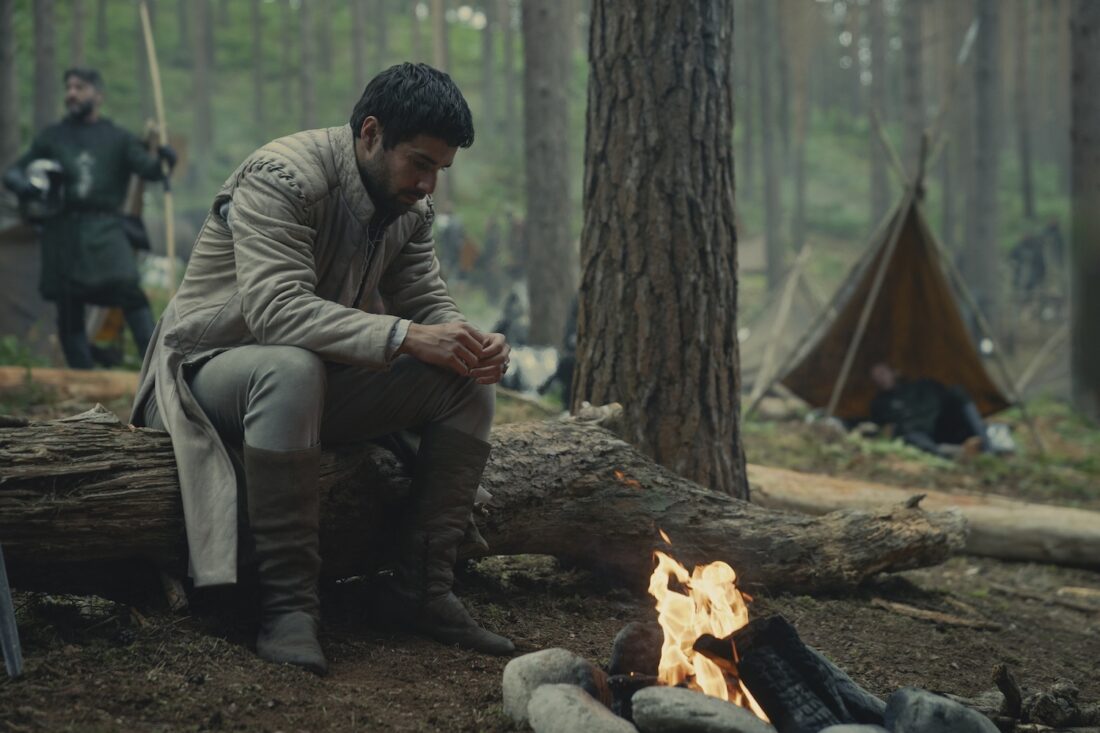 A scene from House of the Dragon season 2 episode 8: Ser Criston Cole (Fabien Frankel) sits on a log beside a camp fire