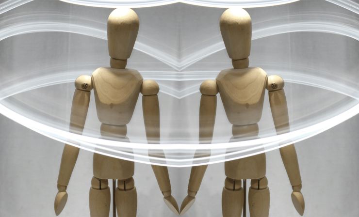 wooden artist's mannequin surrounded by trails of light. The photo is mirrored to create the two mannequins with their hands touching.