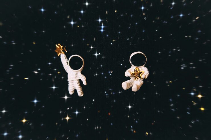 two astronaut figurines holding gold stars, floating against a field of distant stars