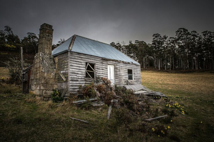 Photo of a dilapidated single story wooden house with a stone chimney