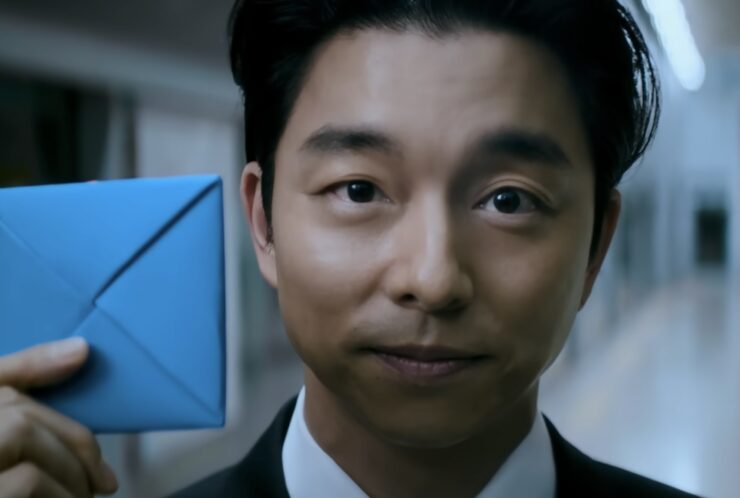 Gong Yoo in Squid Game season 2, holding a blue emvelope aloft