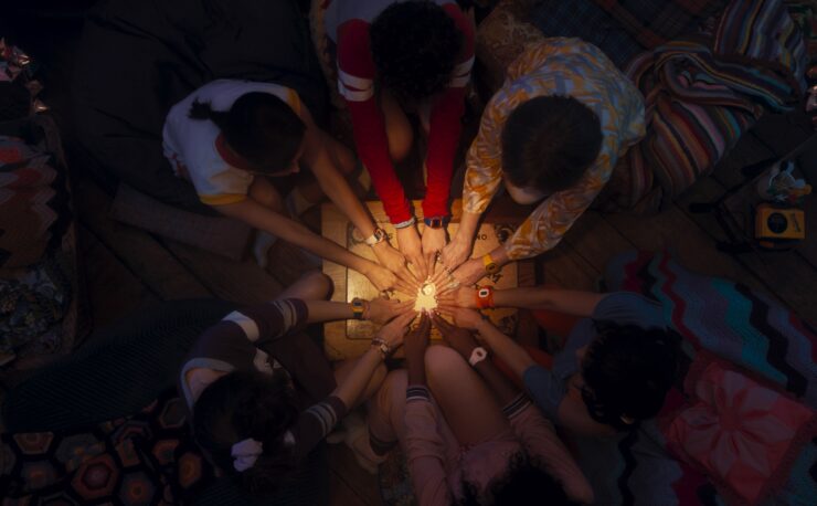 (Clockwise from top left): Rio Vidal (Aubrey Plaza), Teen (Joe Locke), Lilia Calderu (Patti LuPone), Alice Wu-Gulliver (Ali Ahn), Jennifer Kale (Sasheer Zamata), and Agatha Harkness (Kathryn Hahn) with all hands on the planchette of the Ouija board in Agatha All Along, episode 5