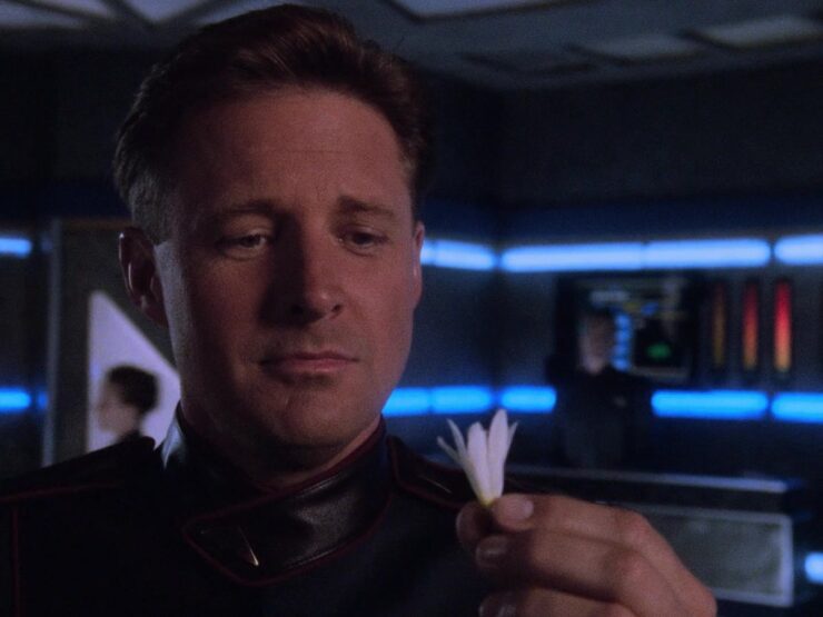 Commander Sheridan holds a small white flower bud in a scene from Babylon 5, "The Geometry of Shadows"