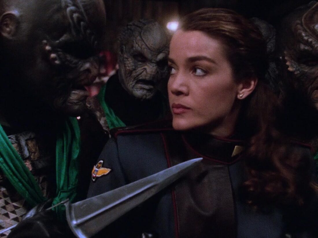 Ivanova is held at knife-point by a group of aliens in a scene from Babylon 5, "The Geometry of Shadows"