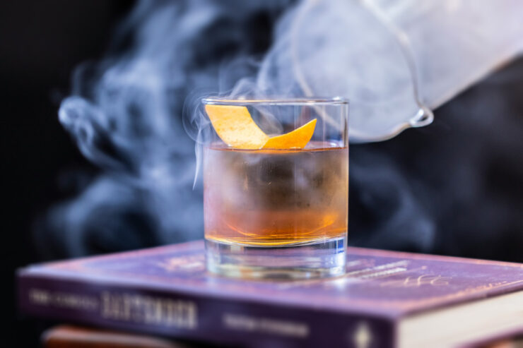 Photo of a cocktail on a stack of books, surrounded by smoke.