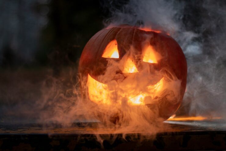 Photo of a lit jack o'lantern against a black background, surrounded by fog or smoke.