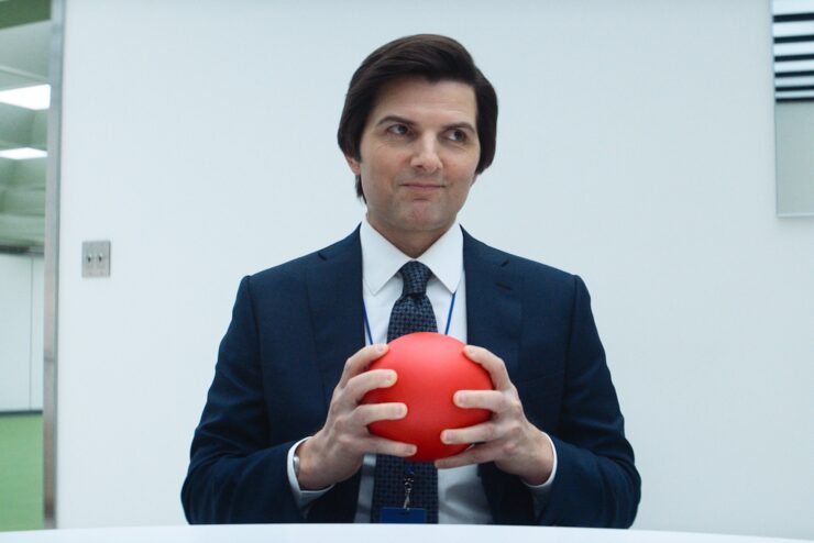 Adam Scott holding a red ball and smirking in Severance Season 2