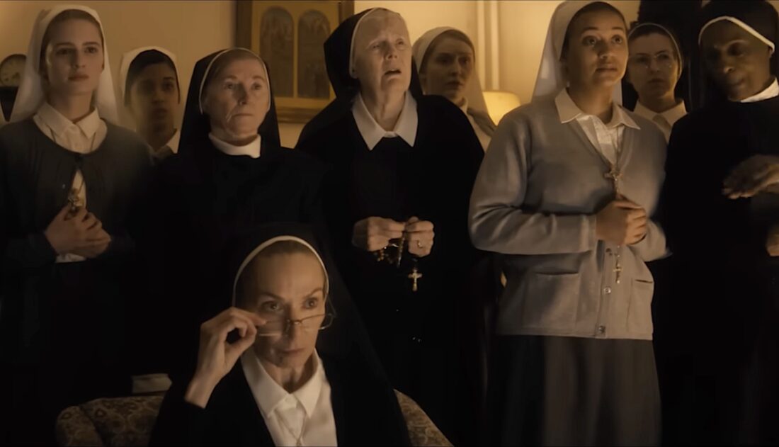 A group of nuns led by Sister Maura (Elizabeth Marvel) watch Margaret Fairchild (Emily Blunt) talk about aliens on television in Disclosure Day.